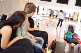 A group of people are sitting in a bowling alley watching a woman bowl.