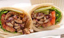 A close up of a chicken wrap with tomatoes , lettuce and onions on a plate.