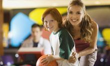 A woman and a boy are bowling together at a bowling alley.