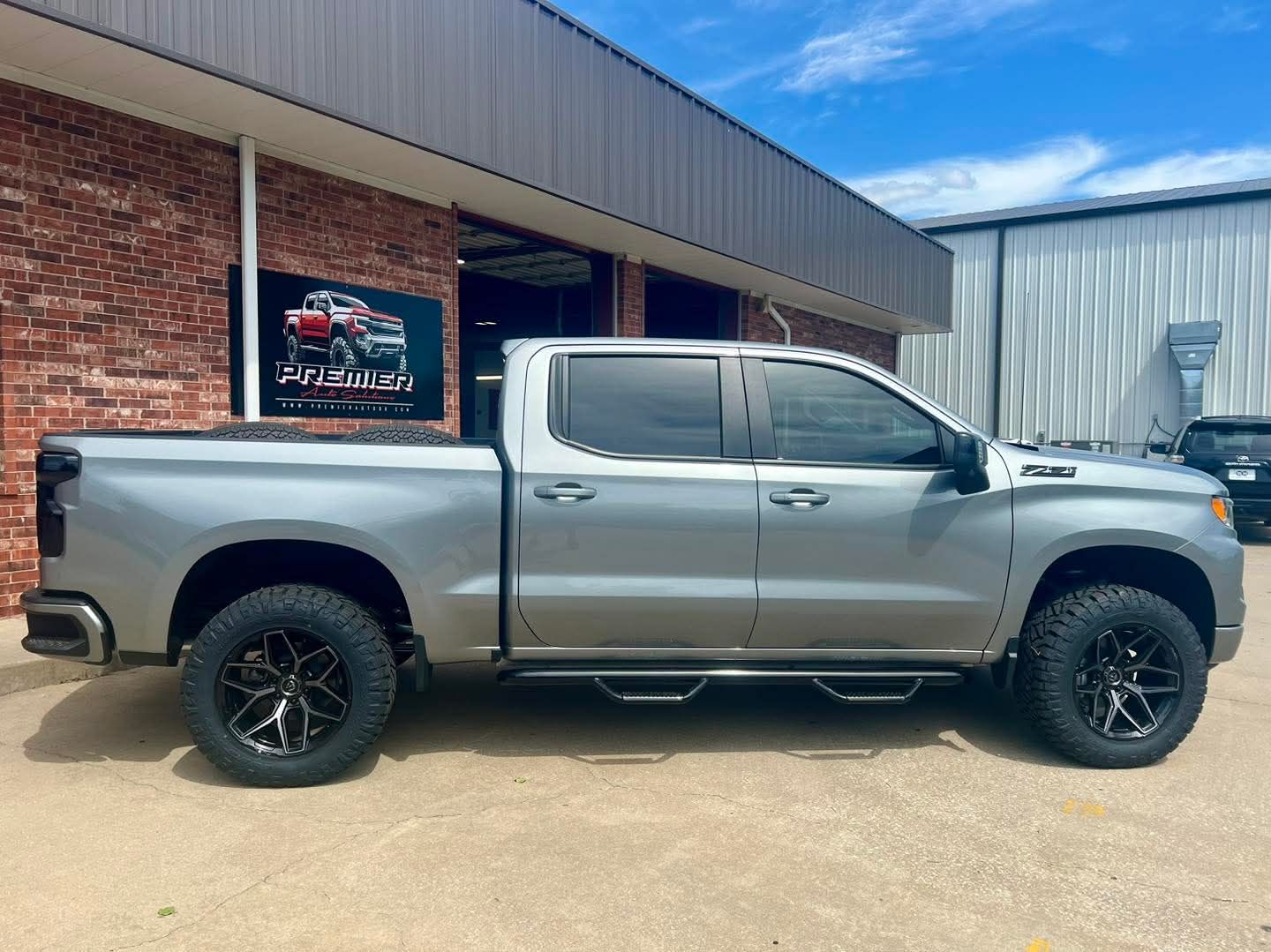Silver lifted pickup truck parked beside a brick building outdoors