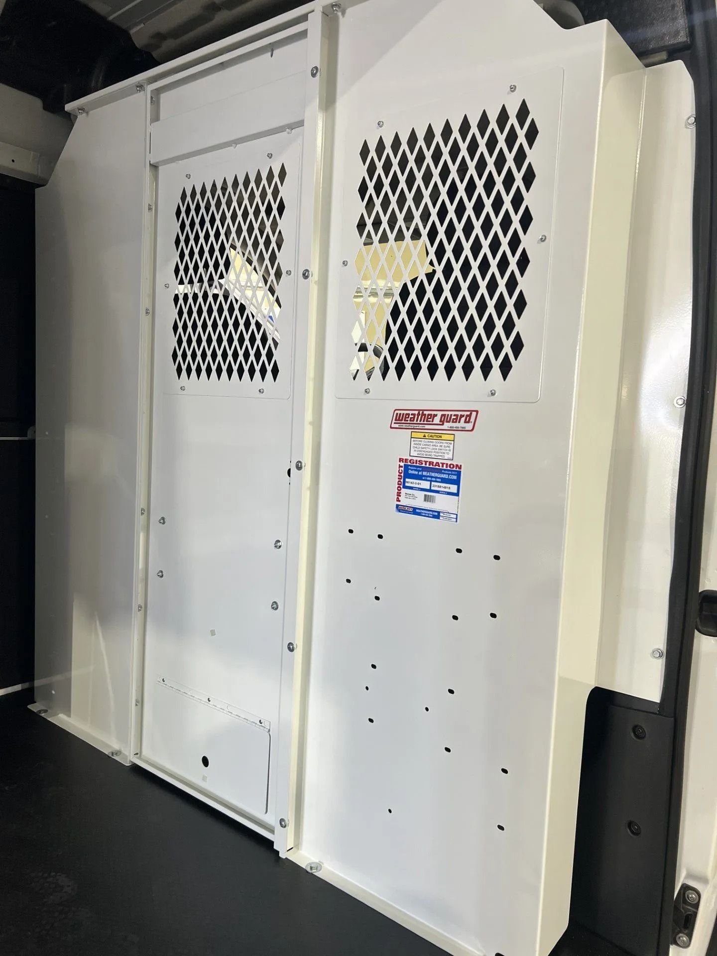 White metal service gate panels with diamond vents and a small warning sign in a hallway