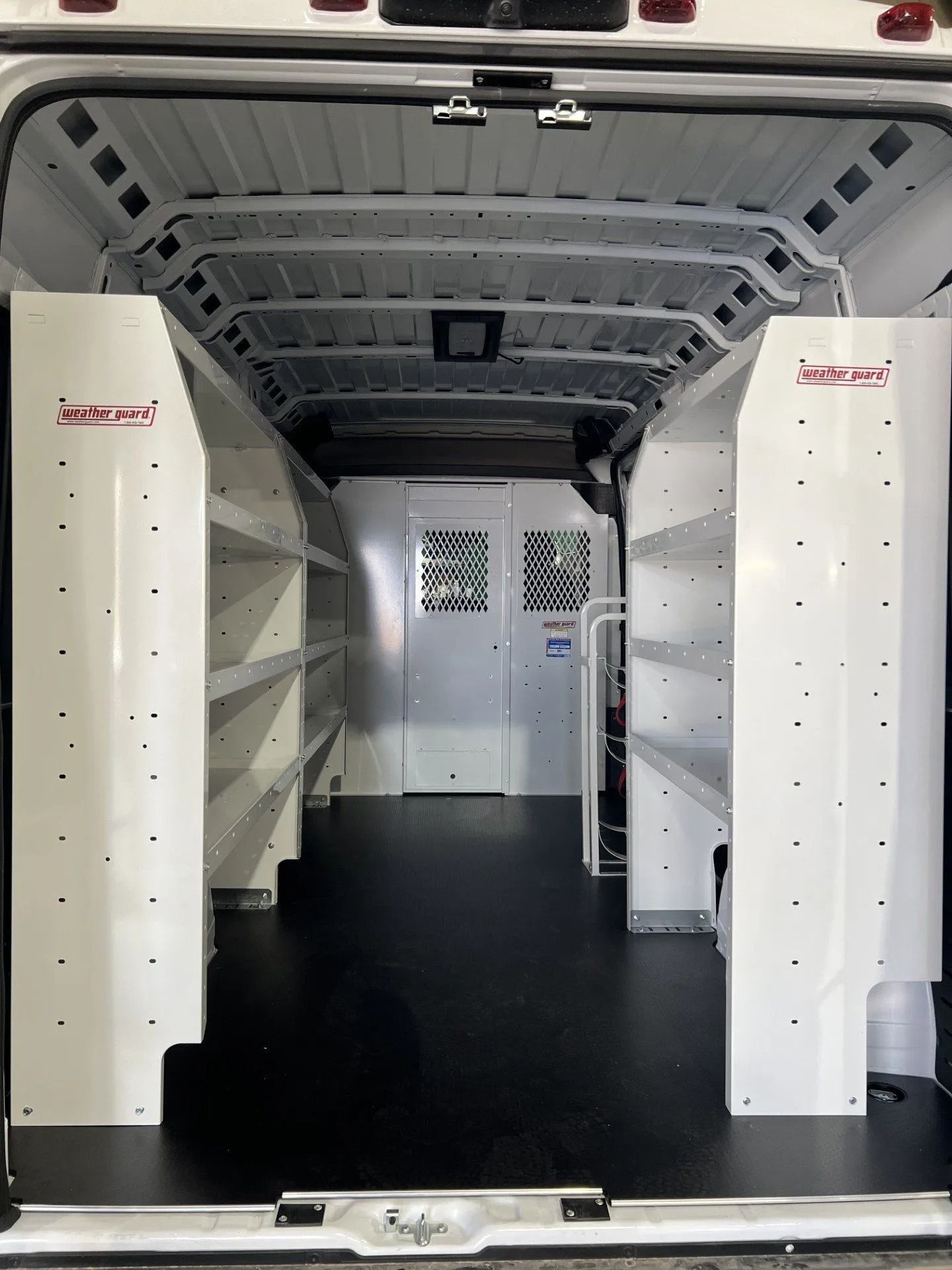 Empty delivery van interior with white shelves and a black floor, viewed from the open rear doors