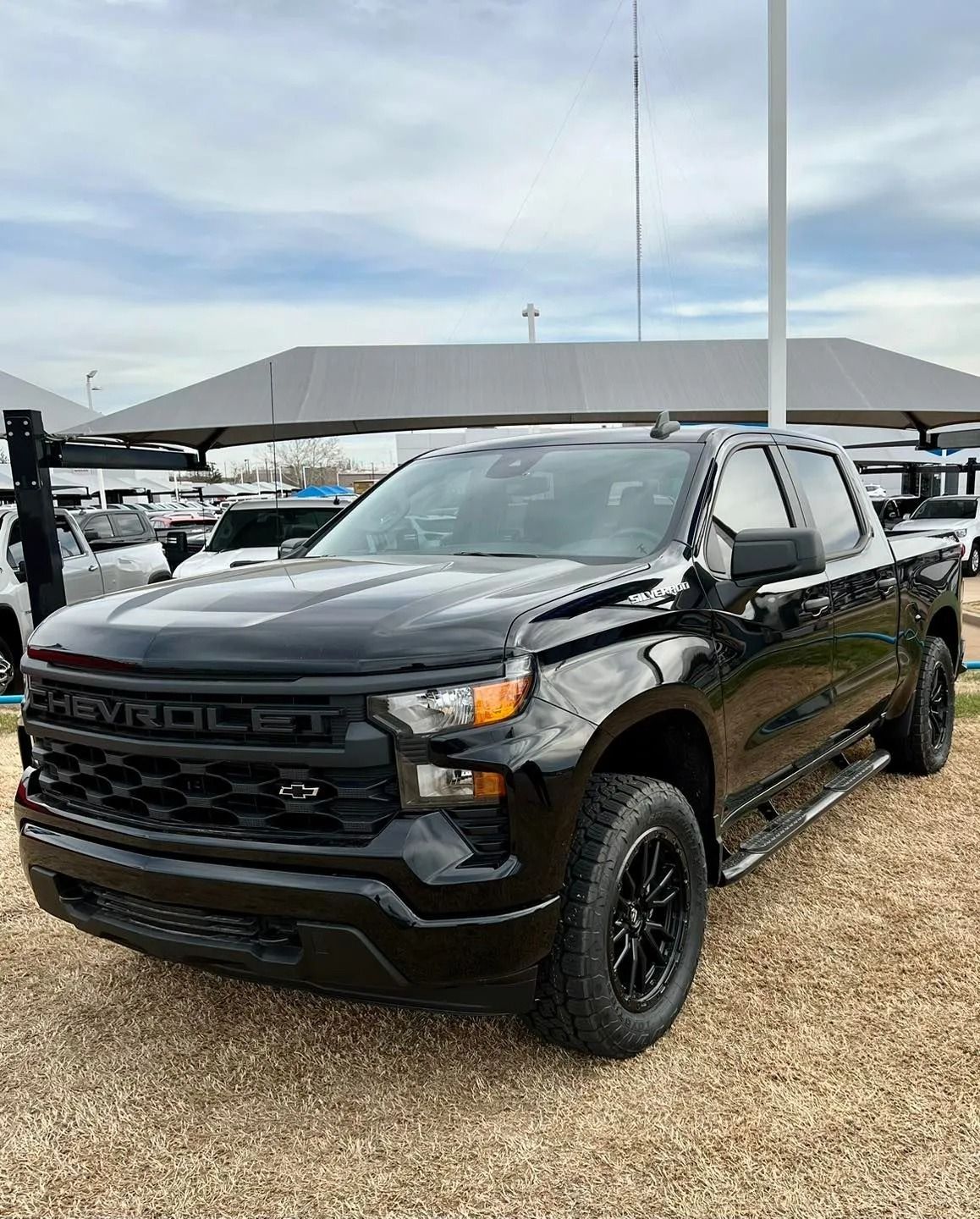 Black Chevrolet pickup truck parked on gravel under a carport at an outdoor lot