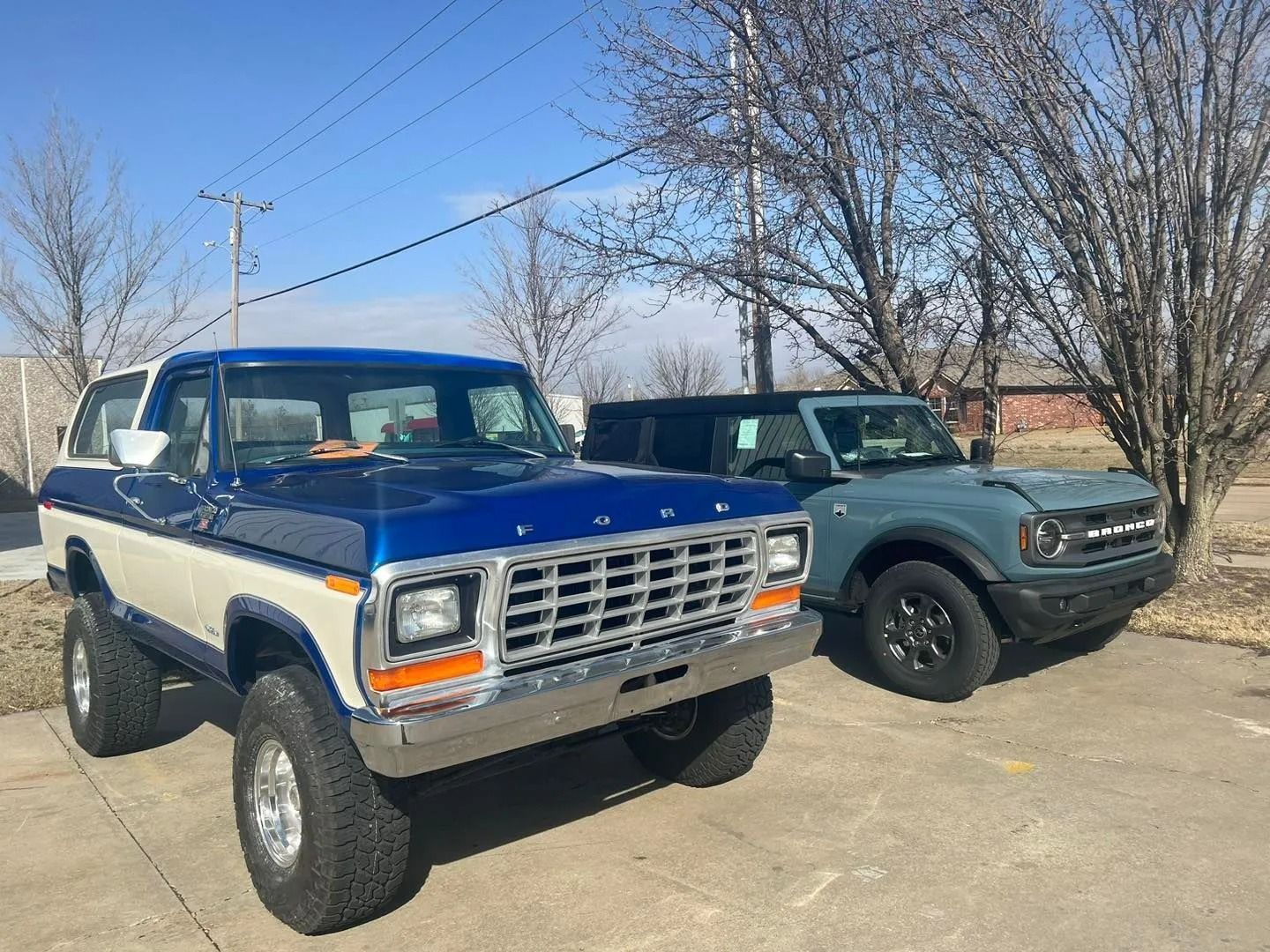 Two vintage pickup trucks parked outdoors under a clear blue sky, one blue and white, one dark green.