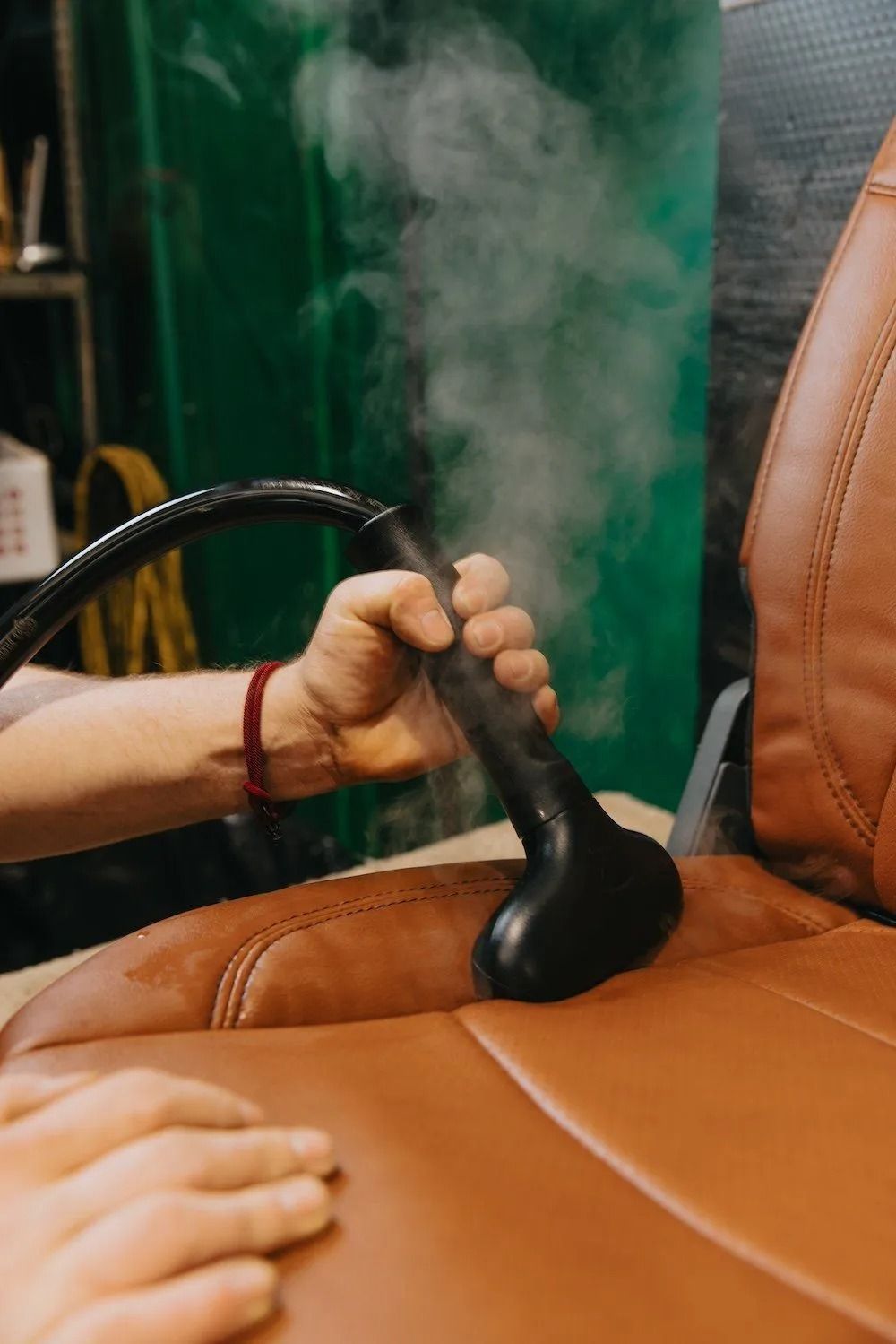 Hand holding a massage tool against a tan leather chair, with steam rising in the background.