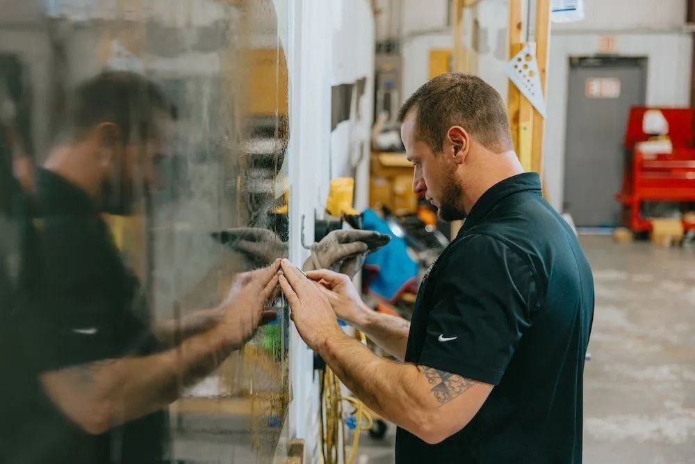Worker inspecting a glass panel in a workshop, with his reflection visible beside him.