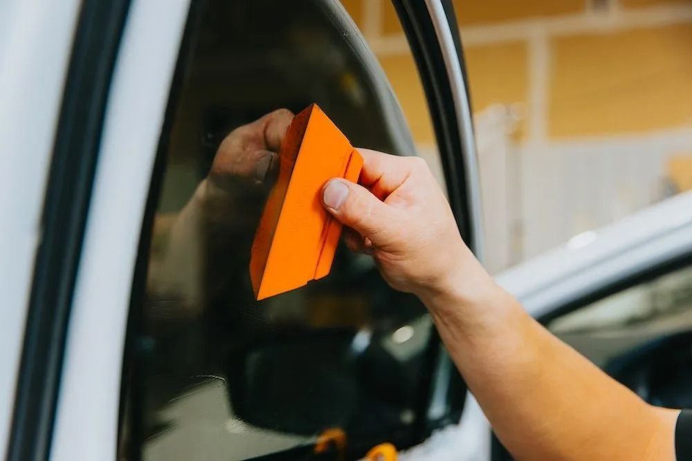 Hand holding an orange squeegee against a car window during cleaning
