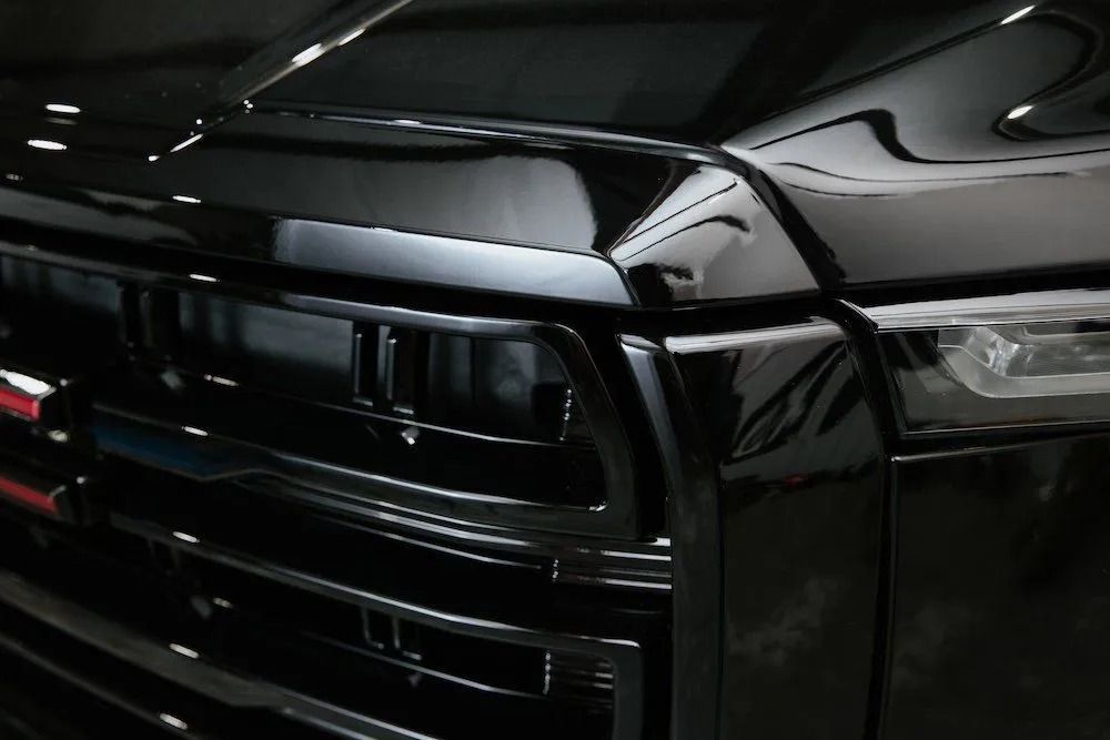 Close-up of a glossy black car front grille and headlight at an angle.