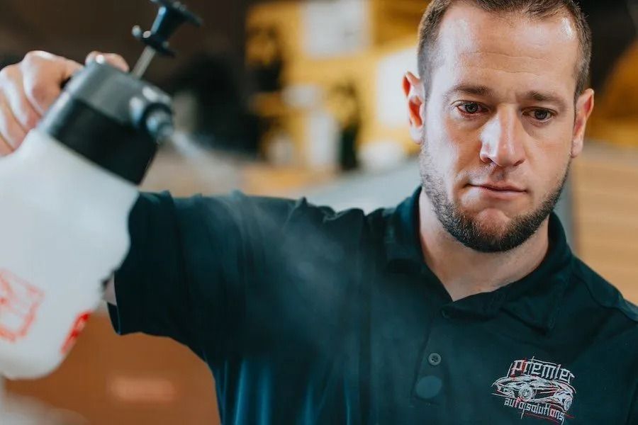 Man in black shirt filling a white spray bottle indoors, looking focused