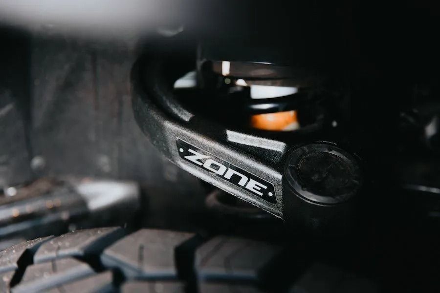 Close-up of a mountain bike suspension fork with ZONE branding and a knobby tire.