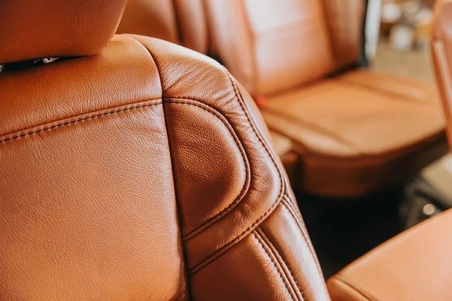 Tan leather car seats with stitched detailing and a blurred rear seat in the background