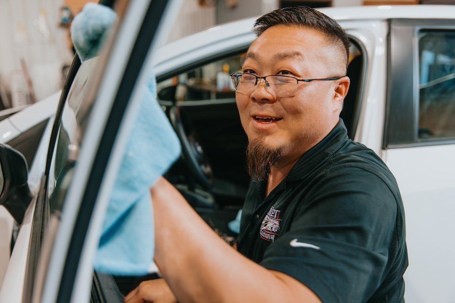 Smiling mechanic in a black shirt working inside a car at a garage