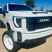 White lifted GMC pickup truck with off-road tires, parked outdoors in bright sunlight