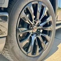 Close-up of a black SUV’s shiny alloy wheel and tire on a sunny street