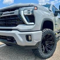 White lifted pickup truck with black wheels parked outdoors under a blue sky