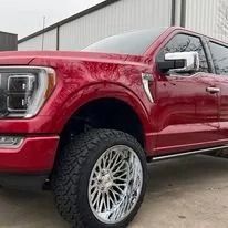 Red pickup truck with large chrome wheels parked outside a building.