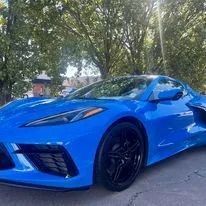 Bright blue sports car parked on a tree-lined street, viewed from the front-left side