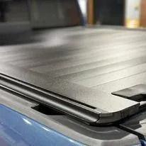 Close-up of a black hard tonneau cover folded on a blue pickup truck bed