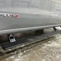 Gray truck with deployed running boards parked on wet pavement