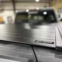 Black tonneau cover on a pickup truck bed with a small badge, in an indoor garage.