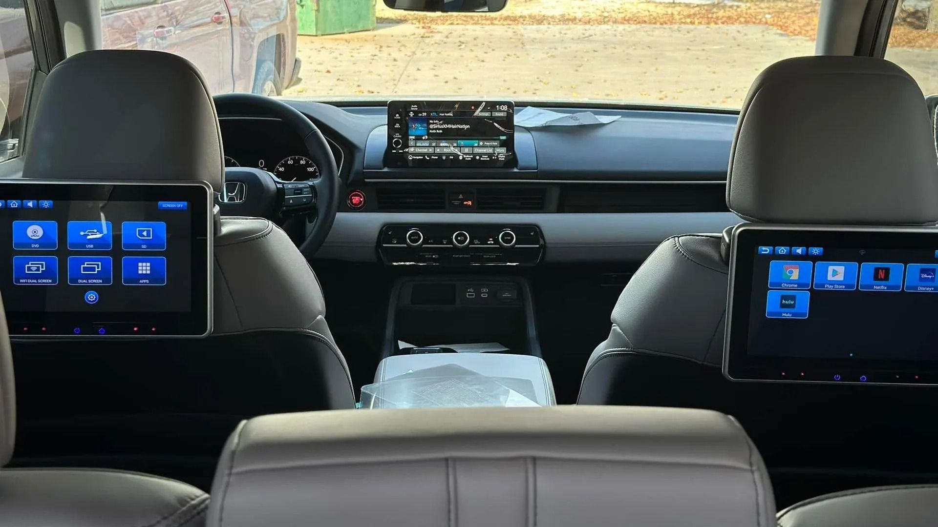 Inside a car, dual rear entertainment screens glow blue behind the front seats.