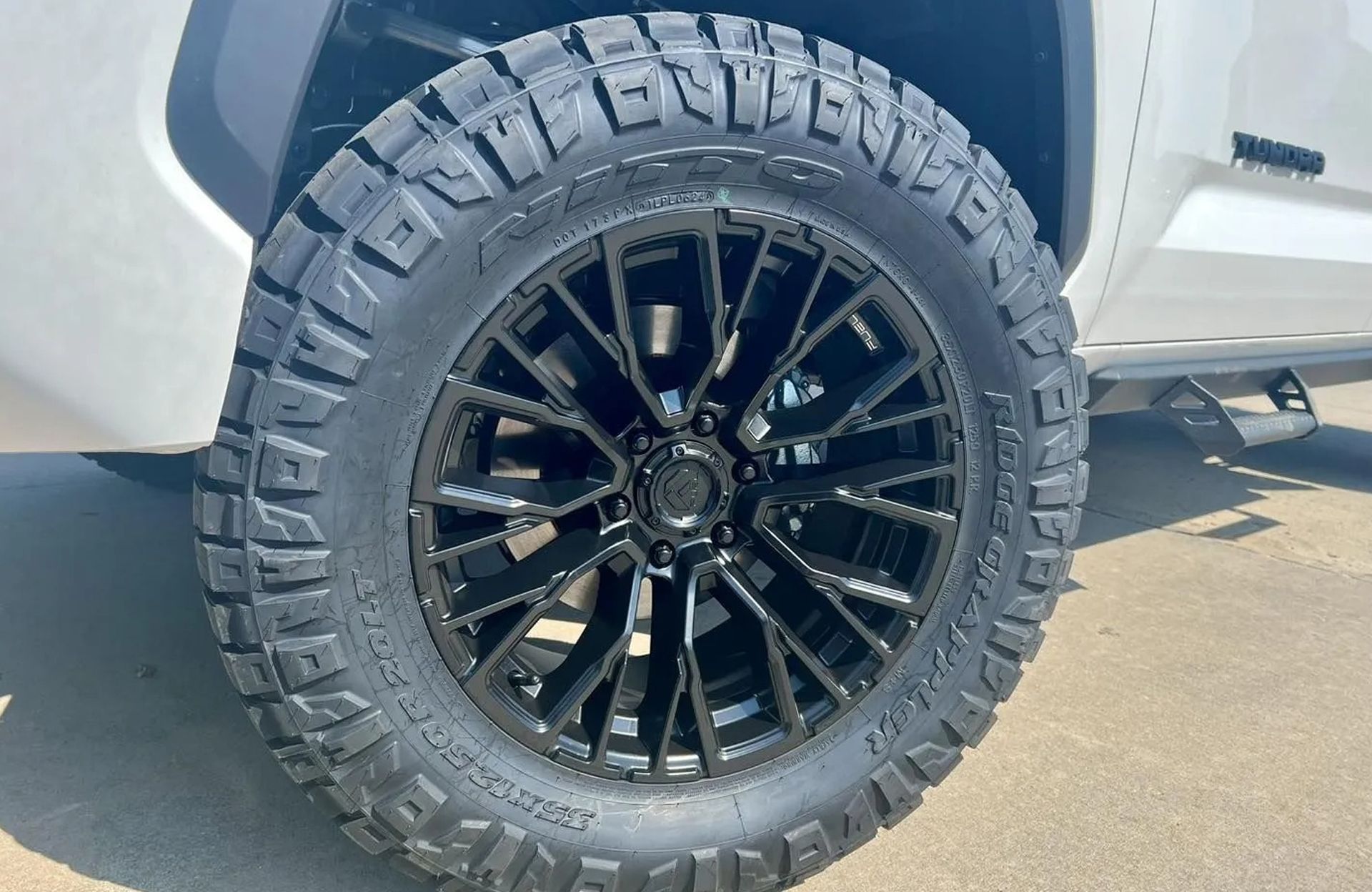 Black off-road truck wheel with rugged tire on a white vehicle outdoors
