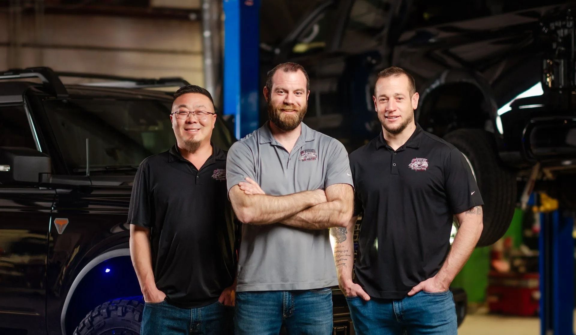 Three men standing in a garage with vehicles, posing for the camera.