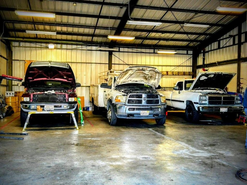 Three trucks are parked in a garage with their hoods open.