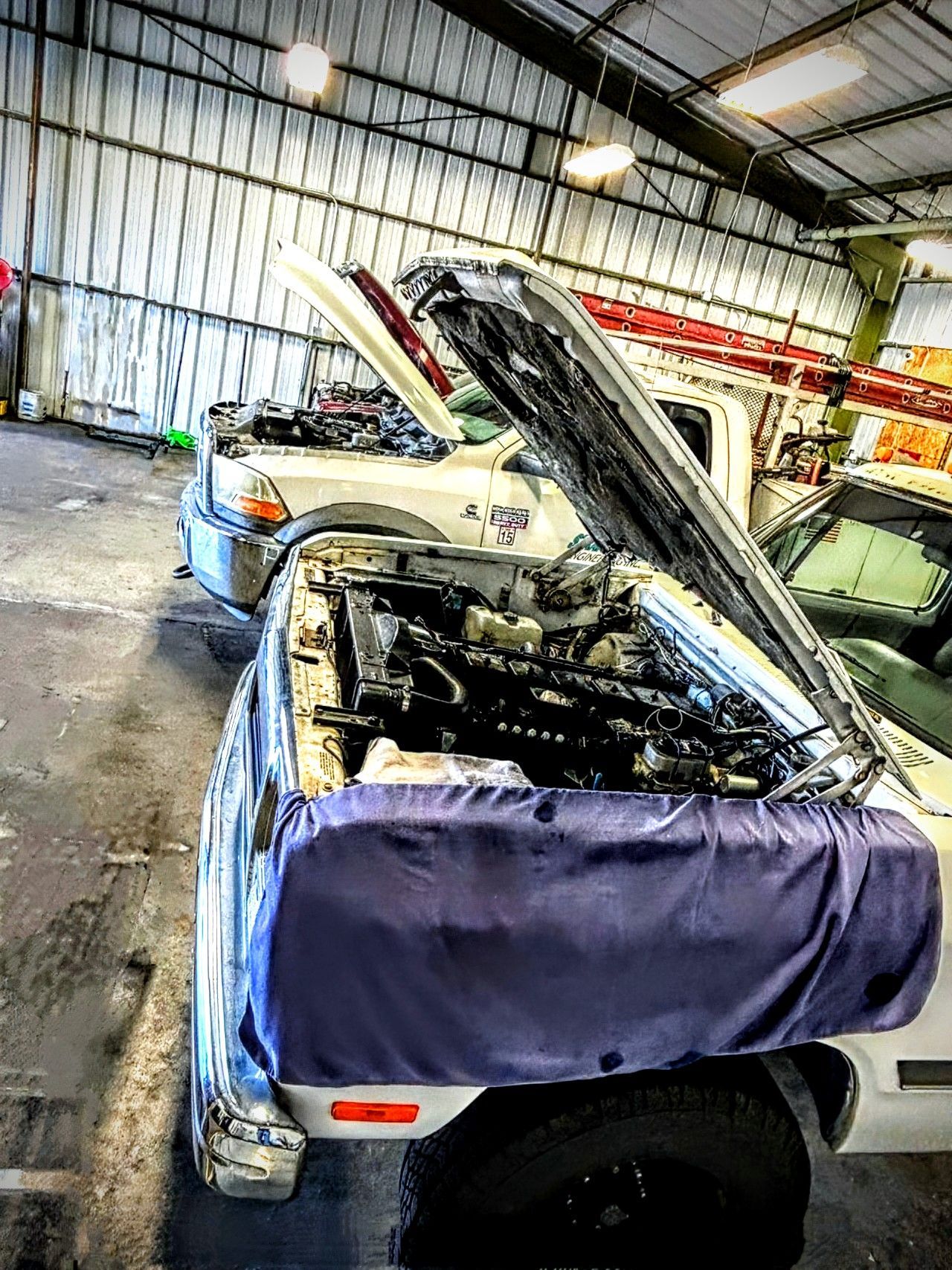 A truck is being worked on in a garage with the hood up.