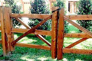 A wooden fence with a gate in the middle of a lush green field.