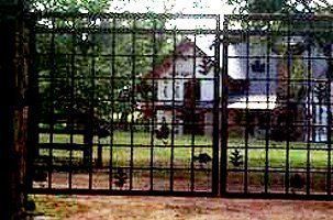 A wrought iron gate with a house in the background behind it.