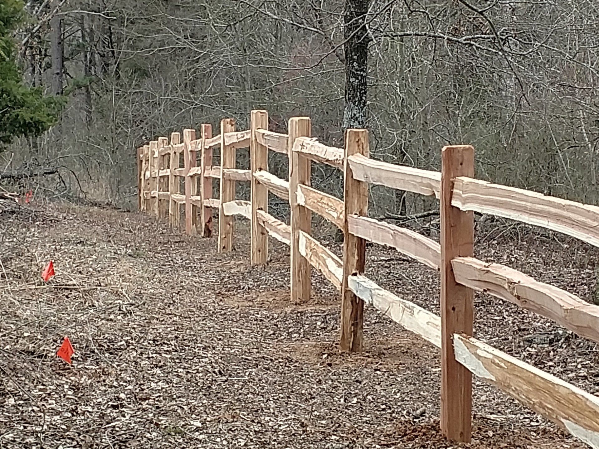 A wooden fence surrounds a dirt path in the woods.