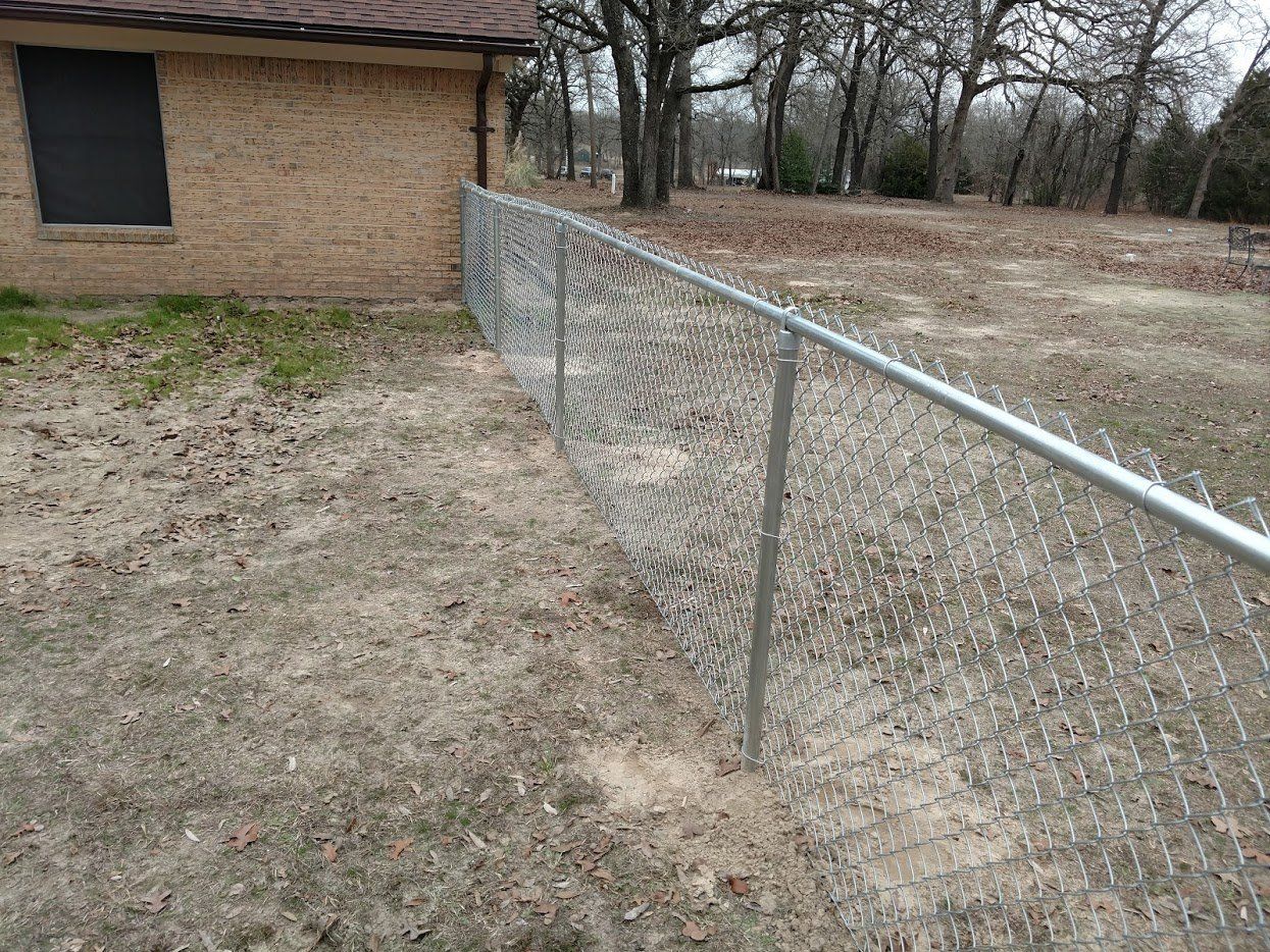 A chain link fence is surrounding a dirt yard in front of a brick house.