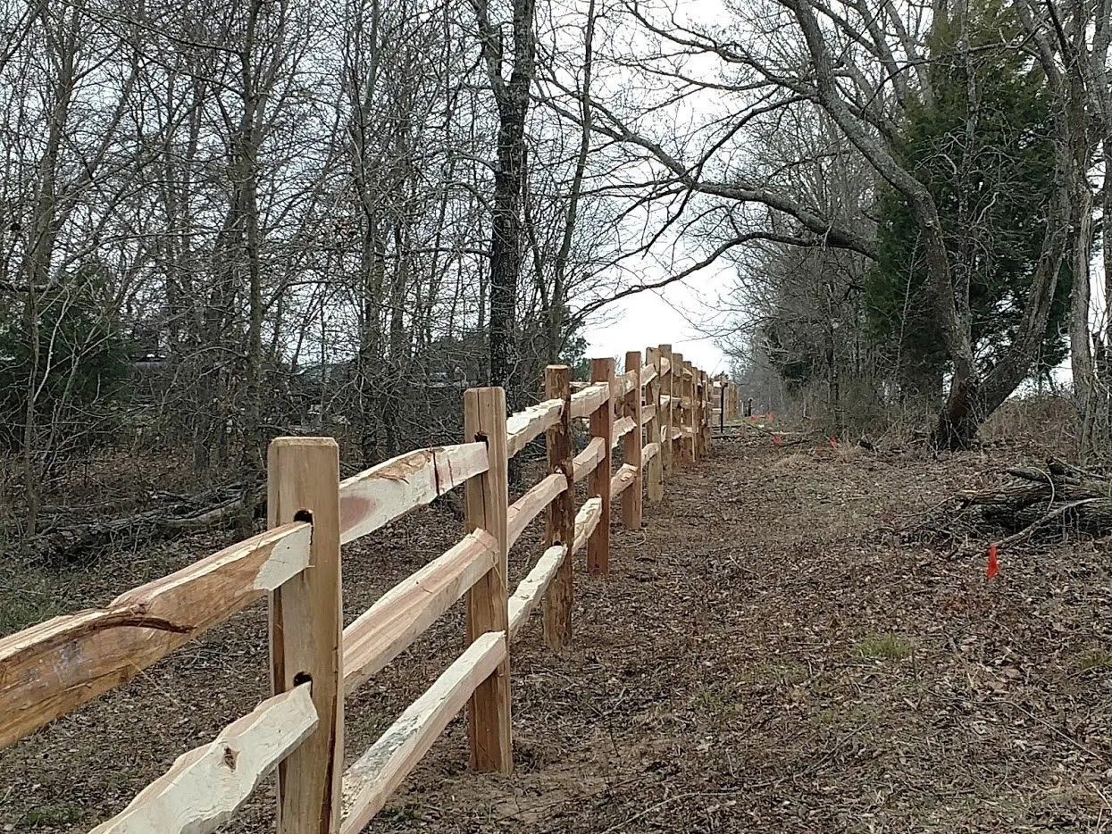 A wooden fence along a path in the woods.