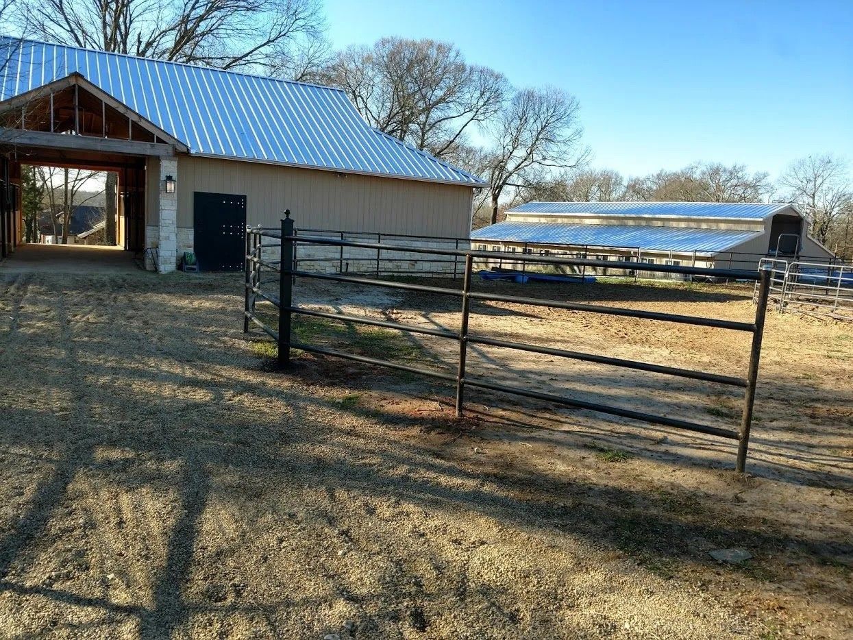 A barn with a metal roof and a fence in front of it.