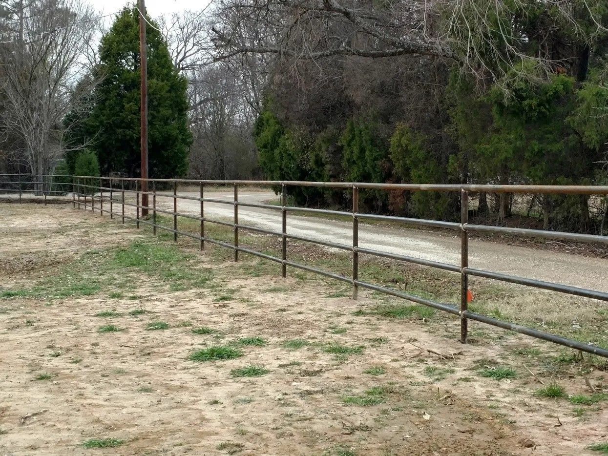 A metal fence surrounds a dirt road in a field.