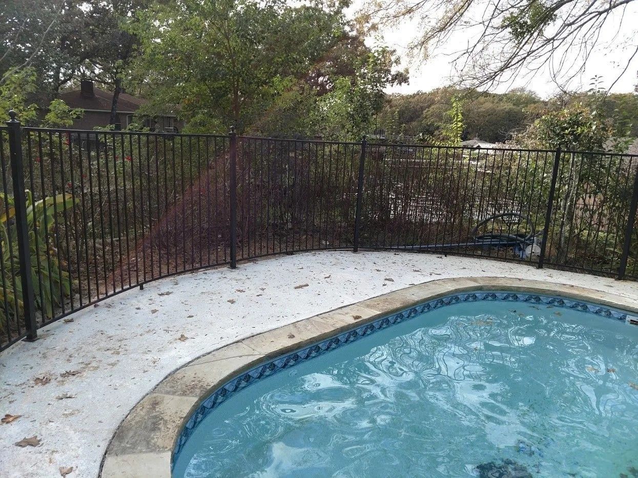 A swimming pool with a metal fence around it and trees in the background.