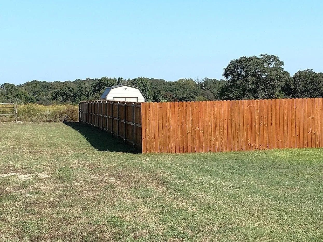 A wooden fence is in the middle of a grassy field.