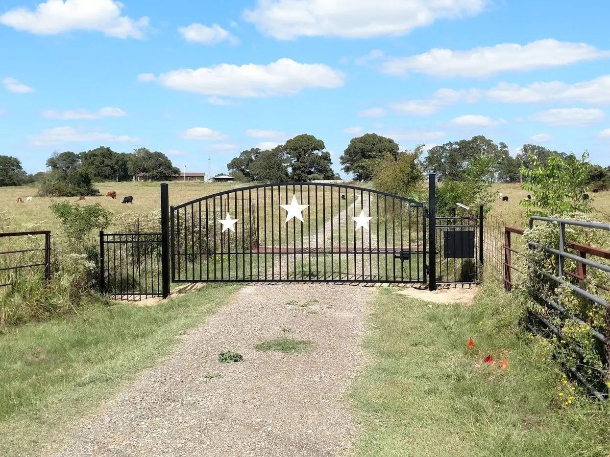A metal gate with three stars on it is in the middle of a dirt road.
