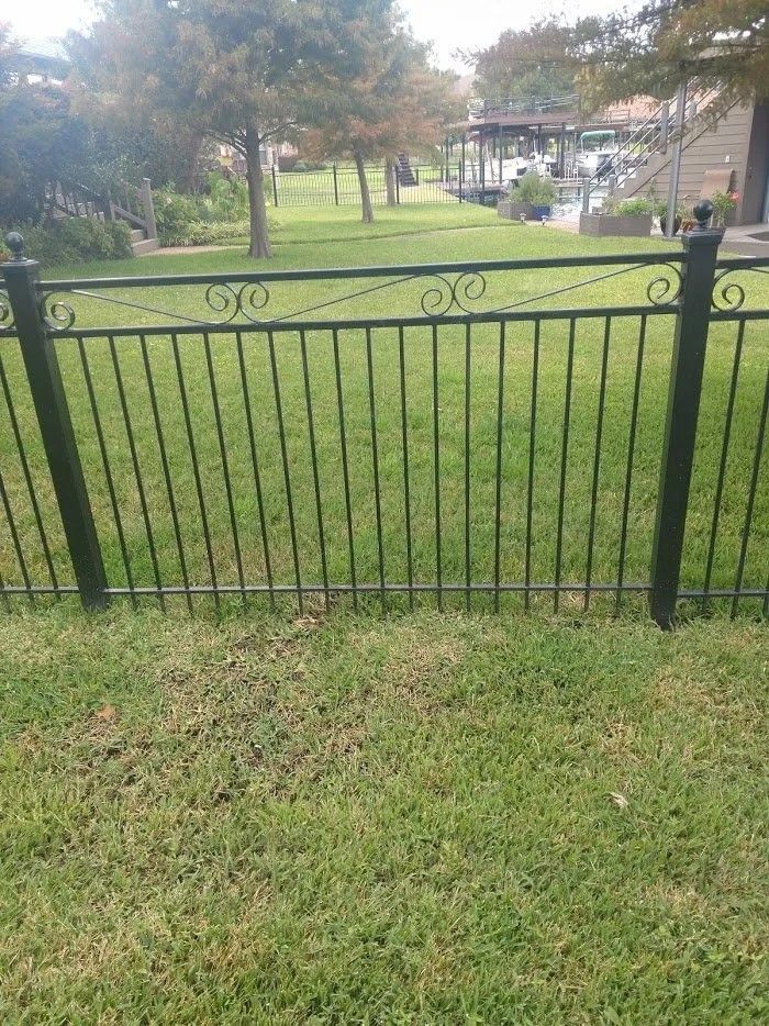 A black fence surrounds a lush green field in a park.