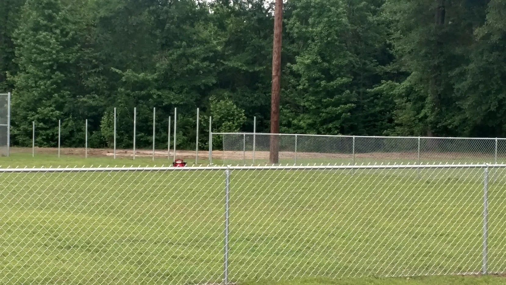 A chain link fence surrounds a baseball field with trees in the background.