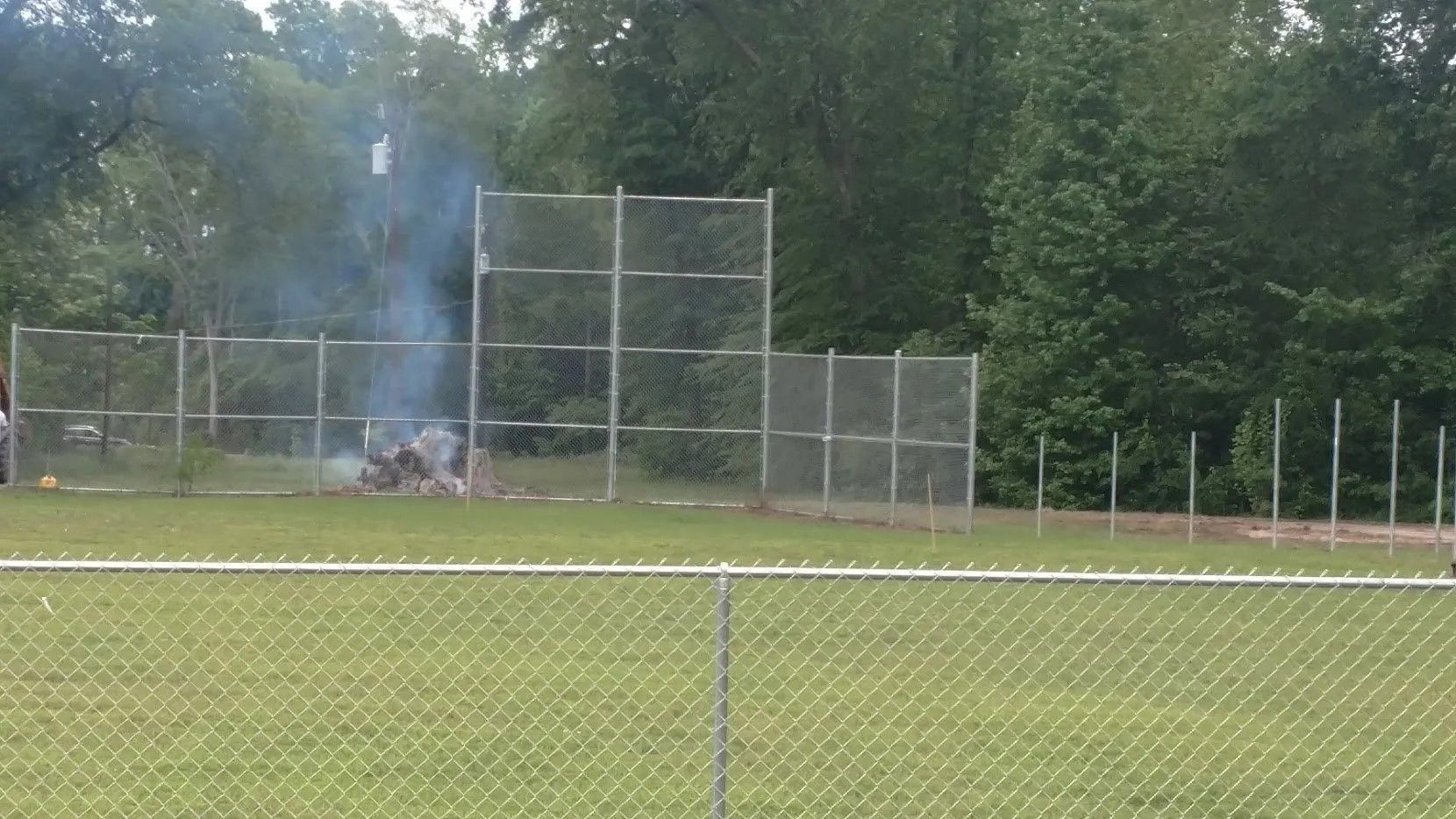 A baseball field with a chain link fence and trees in the background.