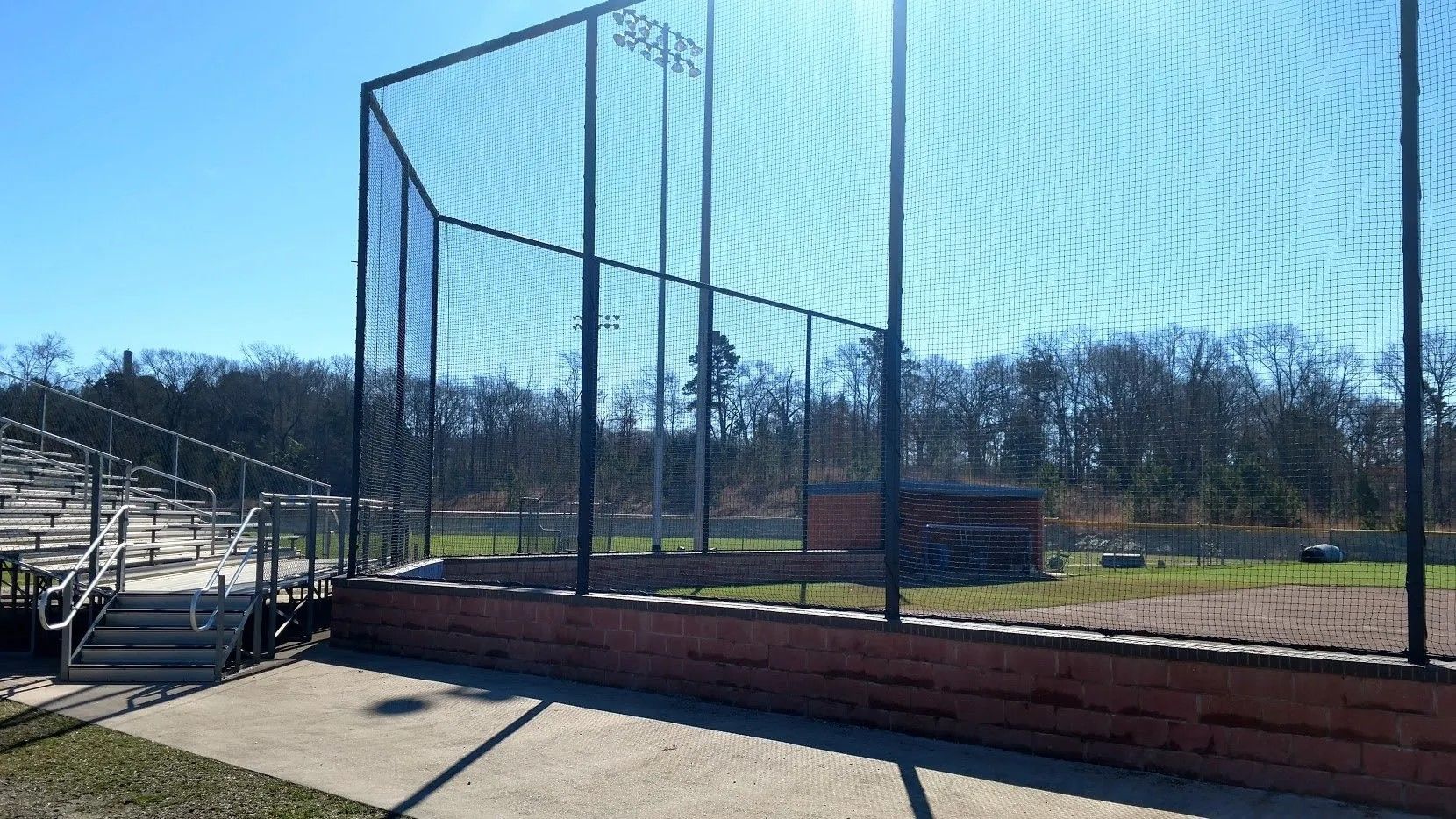 A baseball field with a fence and bleachers in the background.