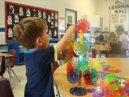 A young boy is playing with a toy in a classroom with a learning wall behind him