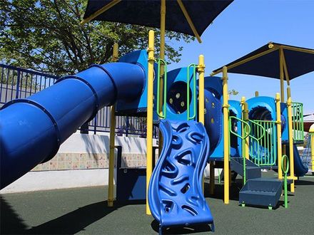 A playground with a blue slide and a yellow umbrella