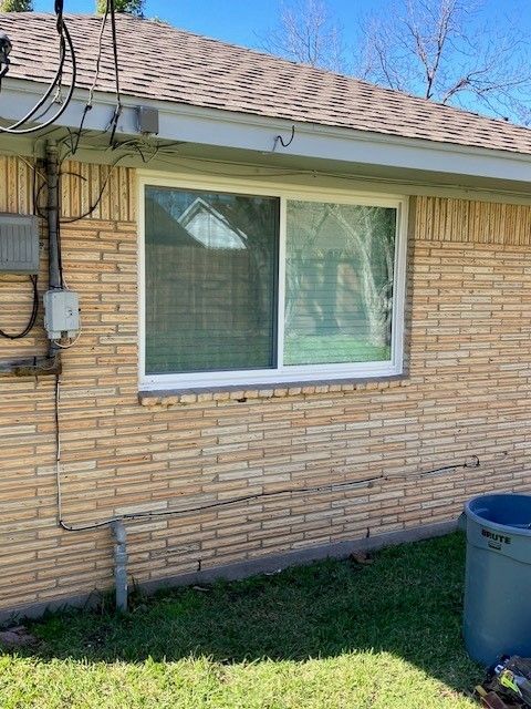 A brick house with a large window and a trash can in front of it.