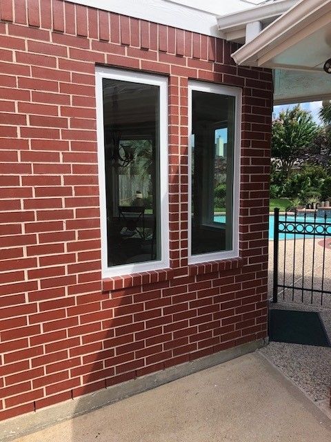 A brick building with two windows and a pool in the background