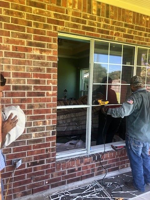 Two men are working on a window on a brick wall.