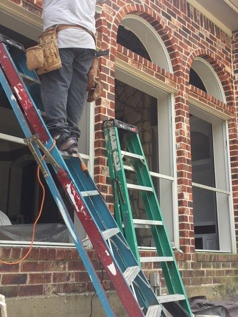 A man is standing on a ladder in front of a brick building