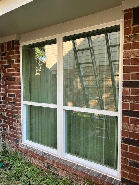 A white window on a brick wall with a ladder in the background.